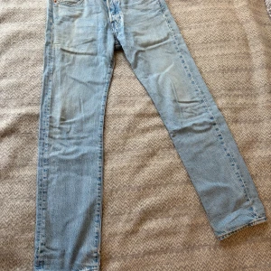 Levi's 501 ljusblå jeans W28 L32 - Ljusblå Levi's 501 jeans med klassisk rak passform och fem fickor. Jeansen har knappgylf och är tillverkade i slitstarkt bomullsmaterial. Perfekt för dig som gillar tidlös denimstil och vill ha ett par jeans med ikonisk look.