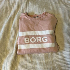 Rosa sweatshirt från Björn Borg - Säljer en snygg rosa sweatshirt från Björn Borg med vit logga framtill. Tröjan har rund halsringning, långa ärmar och är gjord i mjuk bomull. Perfekt för en chill och sportig look.