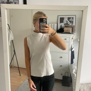 Ljusgrå ärmlös polotopp - Säljer en stilren ljusgrå polotopp utan ärmar. Toppen har en hög krage och är i ett mjukt, stretchigt material som sitter snyggt på kroppen. Perfekt att matcha med jeans eller kjol för en clean look.