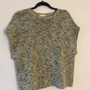 Stickad kortärmad tröja i ljus grön och grå nyanser - En chill stickad tröja med korta ärmar i en mix av grå och ljusgröna toner. Tröjan har en rund halsringning och ett melerat mönster som ger en avslappnad vibe. Perfekt för lager-på-lager och funkar året runt. Materialet är mjukt och stickat för extra komfort.