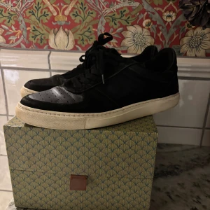 Svarta Filippa K sneakers i mocka och skinn - Snygga svarta sneakers med ovandel i mocka och detaljer i skinn. Skorna har klassisk snörning och en vit platt sula som ger en clean look. Perfekta för dig som gillar minimalistisk stil och vill ha ett par stilrena skor till vardags.