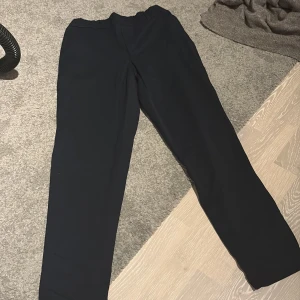 Svarta kostymbyxor från Vero Moda XS - Svarta kostymbyxor från Vero Moda i storlek XS. Byxorna har rak passform, resår i midjan och diskreta fickor bak. Materialet är mjukt och känns skönt mot huden, perfekt för en clean och stilren look.