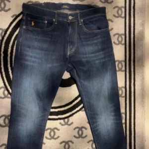 Blå jeans från Polo Ralph Lauren W30 L30 - Snygga blå jeans från Polo Ralph Lauren med klassisk gul broderad logga på fickan. Jeansen har raka ben, fem fickor och kontrastsömmar. Materialet är slitstarkt denim i bomull och passformen är normal. Perfekt för dig som gillar stilrena och tidlösa jeans. Oanvända W30 L30
