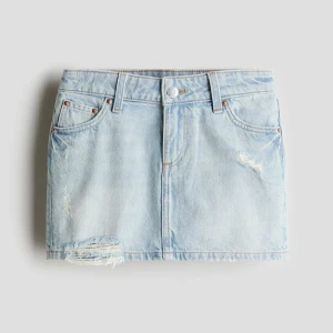 Ljusblå jeanskjol med slitningar - Ljusblå denimkjol i kort modell med snygga slitningar och fransad nederkant. Klassisk femficksdesign, bälteshällor och dragkedja framtill. Helt ny med lapp forfarande kvar.