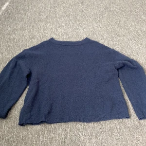 Mörkblå stickad tröja från 157 - Mysig mörkblå stickad tröja från 157 med rund halsringning och långa ärmar. Tröjan har en enkel och klassisk design med ribbade muddar vid hals, ärmslut och nederkant. Använd få gånger