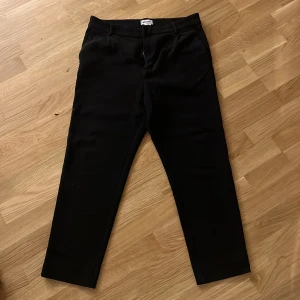Svarta kostymbyxor från Weekday - Stilrena svarta kostymbyxor från Weekday med raka ben och diskreta fickor både fram och bak. Byxorna har en klassisk midja och är sydda i ett mjukt, vävt material som ger en snygg och clean look. Perfekta för dig som gillar minimalistisk stil.