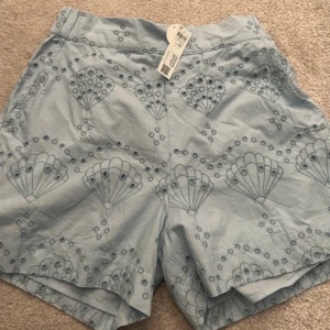 Ljusblå broderade bomullsshorts XS - Superfina ljusblå shorts i bomull med broderade detaljer och unikt mönster. De har hög midja, avslappnad passform och elastisk resår bak. 