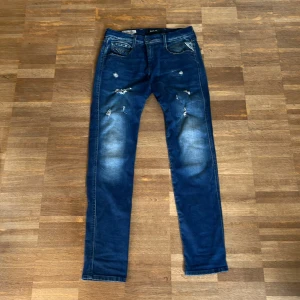 Replay Hyperflex blå jeans, W29 L32 - Snygga Replay Hyperflex jeans i mörkblå tvätt med slitningar och distressed detaljer på framsidan. Modellen är slim och har klassisk femficksdesign, stretchigt material och normal midja. Perfekt för dig som gillar en modern och avslappnad look.