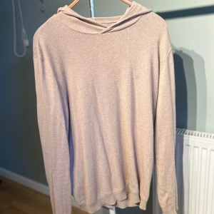 Beige melrinoull hoodie med huva och långa ärmar - Snygg beige melrinoull hoodie med huva och långa ärmar. Tröjan har en enkel och clean design utan mönster eller detaljer, perfekt för dig som gillar en chill och avslappnad stil. Materialet känns mjukt och skönt mot huden, och passformen är normal.