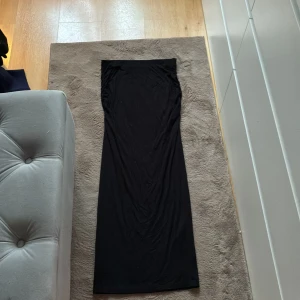 Svart långkjol från Gina Tricot - Svart långkjol från Gina Tricot i mjukt och stretchigt material. Kjolen har en rak och figurnära passform med resår i midjan för extra komfort. Perfekt att styla med en crop top eller oversized hoodie. 