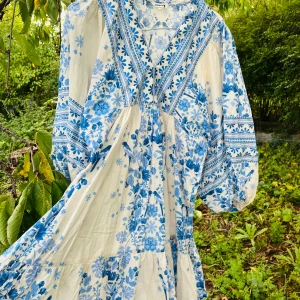 Blåvit blommig långklänning  - Superfin långklänning från indiska  i vitt med blått blommönster. Klänningen har v-ringning, voluminösa långa ärmar 