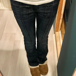 Blå bootcut jeans från Gina Tricot - Snygga blå jeans från Gina Tricot med bootcut passform, stora framfickor, markerade sömmar längs benen och dubbla knappar. Storlek 158, midjemått 38 cm och innerbenslängd 75 cm. 
