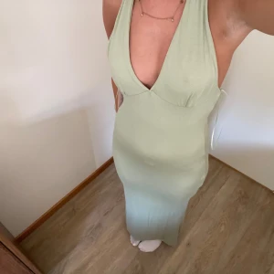 Ljusgrön långklänning med öppen rygg - Supersnygg ljusgrön långklänning med djup v-ringning och öppen rygg. Klänningen har smala axelband som knyts i ryggen och en figurnära passform. Perfekt för dig som vill sticka ut med en stilren och trendig look.