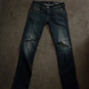 Replay Anbass slim fit jeans blå - Snygga Replay Anbass slim fit jeans i mörkblå tvätt med slitningar på låren. Klassisk femficksmodell med detaljerade bakfickor och läderpatch i midjan. Jeansen har smal passform och är tillverkade i mjukt denimtyg.