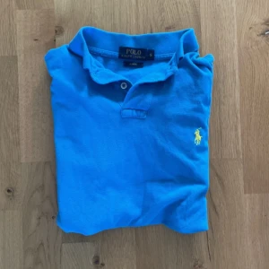 En riktigt snygg blå Pikétröja från Polo Ralph Lauren - Klassisk blå pikétröja från Polo Ralph Lauren  – Small (S) Säljer en stilren och tidlös blå pikétröja i storlek Small. Den är sparsamt använd och i mycket gott skick – inga defekter eller slitage. Perfekt för både vardag och mer uppklädda tillfällen.  Detaljer: 	•	Storlek: Small 	•	Färg: Klarblå med gul logga 	•	Skick: Mycket bra, knappt använd 	•	Pris: 299 kr  Ett kvalitetsplagg som ger en fräsch och välklädd look! 