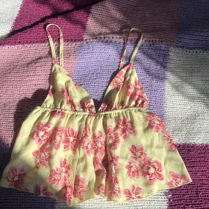 Blommig gul linnetopp från Subdued - Supersöt gul linnetopp från Subdued med rosa blommigt mönster. Topp med tunna, justerbara axelband och v-ringad front. Luftig och flowy passform, perfekt för varma dagar. Använd 1/2 gånger. Köpt för 460kr!