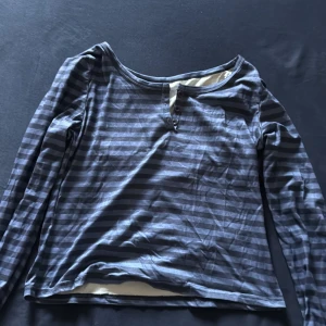 Randig långärmad tröja i grått - Säljer en långärmad tröja med gråa och mörkgråa ränder. Tröjan har rund halsringning med knappdetalj framtill och är tillverkad i ett mjukt bomullsliknande material. Den är storlek Medium men är lite större på.