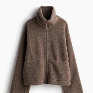 Brun teddyjacka med dragkedja - Mysig brun teddyjacka med hög krage och hel dragkedja framtill. Jackan har två stora fickor och är tillverkad i ett fluffigt teddy-material som håller dig varm under kyliga dagar. Perfekt för dig som gillar en avslappnad och trendig stil.