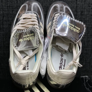 44&42 Adidas Wales Bonner silvriga sneakers - Unika Adidas Wales Bonner sneakers med spegelblankt silverfärgat syntetmaterial, beige detaljer och grova snören. Skorna har stickade ränder på sidorna och mörkbrun sula. Perfekt för dig som vill sticka ut med en futuristisk och trendig look.