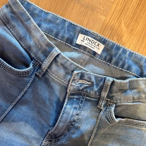 Blå bootcut jeans från Lindex - Snygga ljusblå jeans från Lindex modell Freja med bootcut-modell och markerad söm längs benen. Klassisk femficksdesign och knappstängning framtill. Jeansen har hög midja och är tillverkade i mjukt bomullsmaterial med lite stretch för extra komfort.