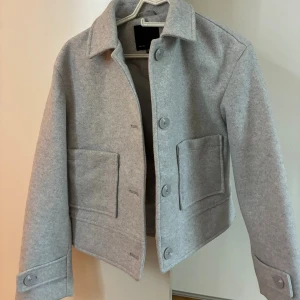 Grå kappa - Stilren grå kappa i storlek XS. Jackan har stora fickor framtill, klassisk krage och knäppning med stora knappar. 🤩