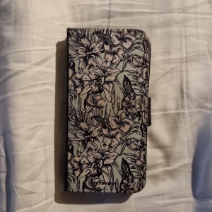 Blommigt svart plånboksfodral till samsung s9 från Bjornberry - Snyggt plånboksfodral från Bjornberry i svart skinnimitation med blommigt mönster på framsidan. Fodralet har plats för kort och ID, magnetstängning och öppning för kamera. Perfekt för dig som vill ha både stil och funktion i ett.