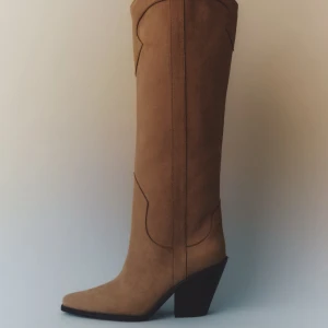 Beiga mocka cowboy boots med klack - Snygga höga cowboy boots i beige mocka med spetsig tå och markerad klack. Stilsäkra sömmar och klassisk western-design gör dem till ett statement. Perfekta för dig som vill sticka ut med en trendig look. Köpta i mars. Använts 2 gånger säljes på grund av för hög klack för min smak. 8,5cm är klacken. Skriv för fler bilder. Finns ej storlekar kvar på hemsidan