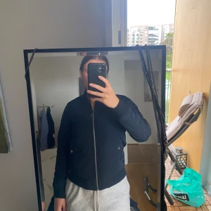 Svart bomberjacka från The Black Label - Säljer en svart bomberjacka från The Black Label Collection i storlek XS. Jackan har quiltade detaljer på ärmarna, ribbade muddar och dragkedja framtill. Snygg och enkel modell som passar till det mesta. Fodrad insida och två fickor med knappstängning.