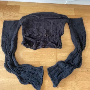 Svart stickad croppad tröja - Svart stickad croppad tröja med långärmade ärmar och hålmönster. Tröjan har en loose passform och är perfekt för lager-på-lager. Snyggt mönster i tyget ger en cool och unik look.