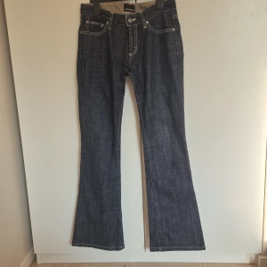 Blå bootcut jeans Calvin Klein - Mörkblå bootcut jeans från Calvin Klein med snygga nitar på bakfickorna. Klassisk femficksmodell med kontrastsömmar och normal passform. Jeansen har låg midja och är tillverkade i slitstarkt denimtyg. De är små runt midjan.
