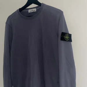 Lila sweatshirt från Stone Island - Säljer en stilren lila sweatshirt från Stone Island med klassisk patch på vänster ärm. Tröjan har rund halsringning och långa ärmar, perfekt för dig som gillar enkel men snygg streetwear. Materialet är mjukt och skönt bomullstyg.