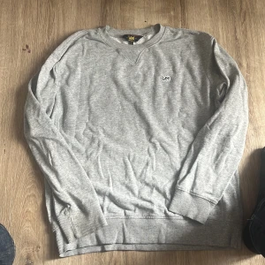 Grå sweatshirt från Lee - Säljer en enkel och stilren grå sweatshirt från Lee i regular fit. Tröjan har rund halsringning, långa ärmar och diskret Lee-logga broderad på bröstet. Perfekt för dig som gillar en clean och avslappnad look.