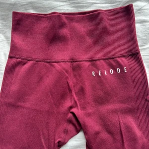 Vinröda leggings från Relode - Snygga vinröda leggings från Relode med hög midja och ribbade detaljer längs sidorna och midjan. Tillverkade i ett stretchigt syntetmaterial som sitter tight och bekvämt. Perfekta för träning eller chill dagar. Aldrig använda 