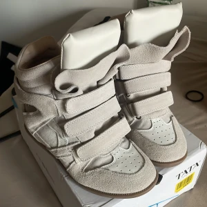 Beige sneakers Isabel Marant - Inte äkta men väldigt snygga! Kan absolut sälja lite billigare men köpte för 2700 så inte mindre än 1500! Snygga beige sneakers med högt skaft och flera breda kardborreband. Skorna har en mix av mocka och skinn, rund tå och platt sula. Perfekta för dig som gillar en sportig men trendig look.