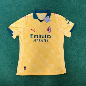 AC Milan 25/26 fotbollströja Puma - AC Milan fotbollströja i gult med subtilt geometriskt mönster. Tröjan har mörkblå krage och ärmslut, röda Puma-loggor och klubbmärke på bröstet. Tillverkad i lätt och ventilerande funktionsmaterial, perfekt för match eller träning.