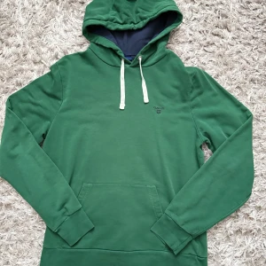 Grön hoodie från GANT med huva - Snygg grön hoodie från GANT med vit dragsko i huva. Mörkblått foder i huvan ger en schysst kontrast. 