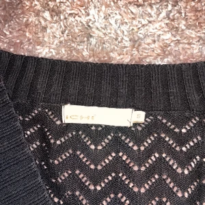 Svart stickad v-ringad tröja ICHI - Svart stickad tröja från ICHI i storlek S. Tröjan har ett snyggt hålmönster i zickzack, djup v-ringning och långa ärmar. Ribbstickade muddar vid ärmslut och nederkant ger en schysst passform. Perfekt för lager-på-lager och stilrena outfits.