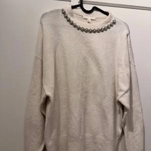 Vit stickad tröja med pärldetaljer  - Superfin vit stickad tröja från H&M i storlek XS. Tröjan har långa ärmar, ribbade muddar och en rund halsringning dekorerad med pärlor och glittriga stenar som ger en lyxig känsla. Perfekt för dig som vill sticka ut lite extra.