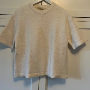 Beige stickad kortärmad tröja - En stilren beige stickad tröja från Gina Tricot med korta ärmar och rund halsringning. Tröjan har ribbade kanter vid ärmslut, hals och nederkant. Perfekt för lager-på-lager och enkel att matcha med olika outfits.
