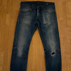 Blå skinny jeans från Lee ”Luke” - Snygga blå jeans från Lee ”Luke” med slitningar och hål på låret och knät. Jeansen har klassisk femficksdesign, smal passform och tydliga tvättade detaljer för en cool look. Perfekta för dig som gillar en lite ruffare stil.