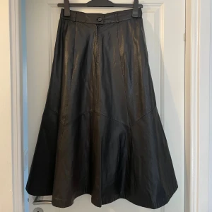 Jofama Svart lång skinnkjol  - Säljer en svart långkjol i äkta skinn från Jofama Trend. Kjolen har en snygg A-linjeform, midjehällor och stängs med knapp och dragkedja framtill. Perfekt för dig som vill ha en edgy och tidlös look. Kjolen är storlek 40-42 ca. Otroligt fin på! Nypris 2800kr.