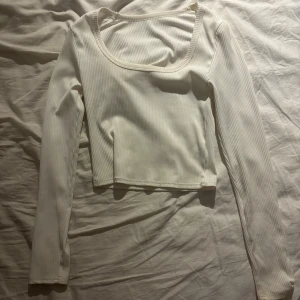 Vit ribbad långärmad croppad topp - Säljer en vit ribbad långärmad topp med croppad passform och fyrkantig urringning. Toppen är i stretchigt material och har en clean, stilren look som passar perfekt till jeans eller kjol. Enkel att styla och superbekväm. iprincip aldrig använd!