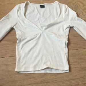 Vit v-ringad topp från Gina Tricot - Säljer en vit långärmad topp från Gina Tricot i storlek XS. Toppen har en snygg v-ringning och figurnära passform, perfekt att styla med jeans eller kjol. Tillverkad i mjukt och stretchigt material för en bekväm känsla.