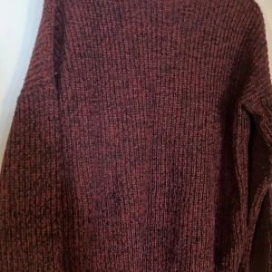 Vinröd stickad tröja från Atmosphere - Mysig vinröd stickad tröja från Atmosphere i storlek 38. Tröjan har en grovstickad struktur och långa ärmar, perfekt för kyliga dagar. Färgen är en blandning av mörkrött och svart som ger en snygg djup ton. Enkel och stilren modell som är lätt att matcha.