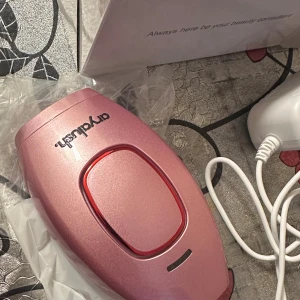 Arydush IPL Hårborttagningsapparat - Effektiv IPL-hårborttagningsapparat i snygg rosa design. Levereras med strömadapter och originalförpackning. Enheten ser ut att vara i mycket gott skick utan synliga defekter eller slitage. Perfekt för smidig och skonsam hårborttagning hemma.