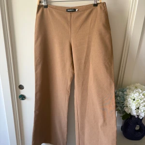 Beiga wide byxor från ONLY - Snygga beiga byxor från ONLY med breda ben och låg midja. Byxorna har en enkel design utan synliga fickor eller detaljer och är tillverkade i ett mjukt bomullsliknande material. Perfekta för en chill och stilren look.