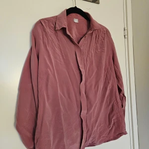 Rosa silkesskjorta - Säljer en jättefin skjorta i 100% silke i en snygg rosa färg. Skjortan har klassisk krage, långa ärmar med knapp vid ärmslut och en avslappnad passform. 