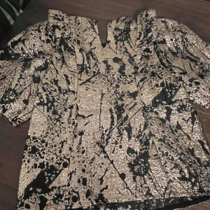 Glittrig topp från Sofie Schnoor - Supersnygg glittrig topp från Sofie Schnoor i svart och guld med unikt abstrakt mönster. Toppen har kort puffärm.