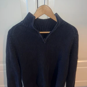 Marinblå stickad tröja Henri Lloyd - Snygg marinblå stickad tröja från Henri Lloyd i storlek S. Tröjan har ribbad struktur, half zip och hög krage. På ärmen finns ett broderat märke med Union Jack och Henri Lloyds emblem. Perfekt för kyliga dagar och stilrena outfits, hör av er vid funderingar! Pris kan diskuteras.
