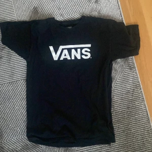 Svart Vans t-shirt med logga - Svart t-shirt från Vans i 100% bomull med klassisk vit Vans-logga tryckt på bröstet. Modellen är kortärmad och har en normal passform. Perfekt för dig som gillar streetwear och enkel stil.